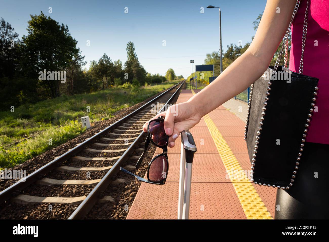 Zugfahrt im Sommer. Eine Frau steht auf dem Bahnsteig und hält eine Sonnenbrille in der Hand. Stockfoto