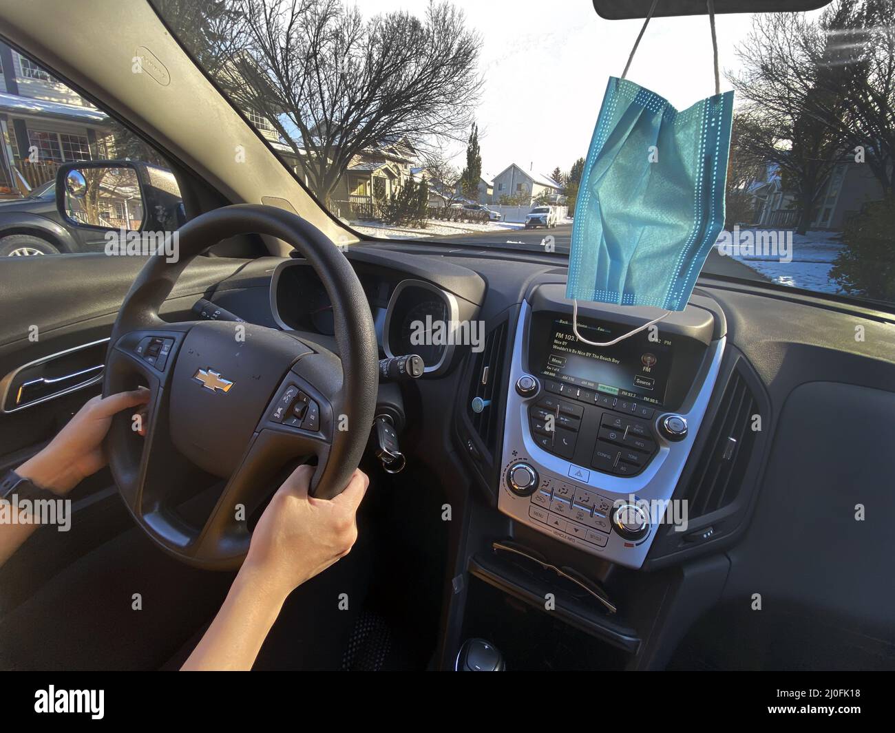 Calgary, Alberta, Kanada. Oktober 17, 2020. Eine Person, die an einem sonnigen Tag ein Chevrolet-Auto fährt, mit einer Gesichtsmaske, die vom Spiegel hängt Stockfoto