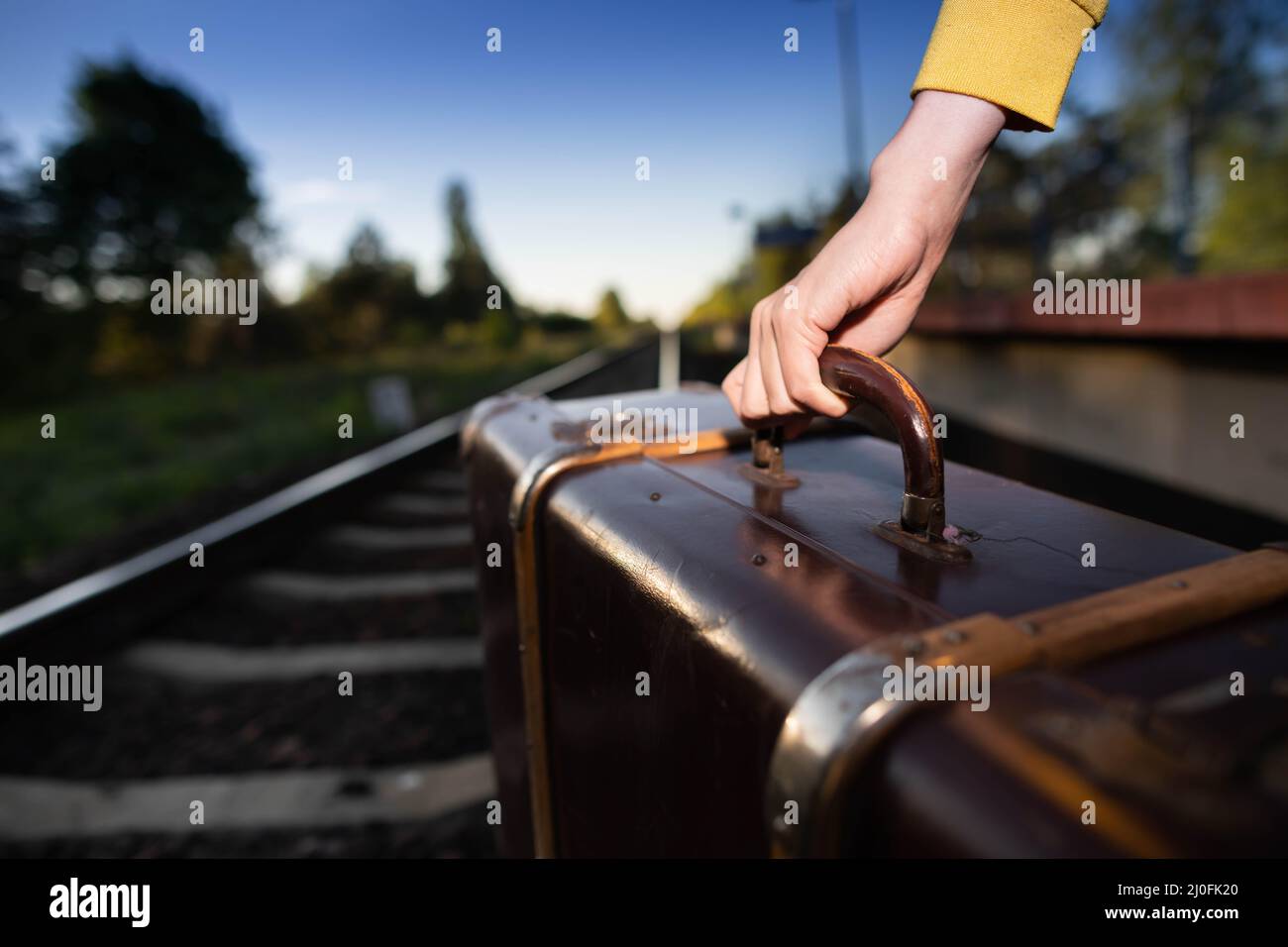 Kein sicherer Spaziergang auf den Schienen mit einem alten Reisekoffer bei Sonnenuntergang an heißen Sommertagen. Stockfoto