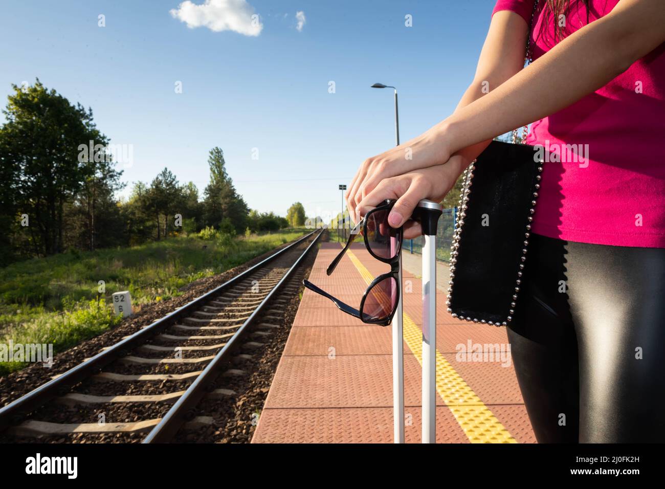 Zugfahrt im Sommer. Eine Frau steht auf dem Bahnsteig und hält eine Sonnenbrille in der Hand. Stockfoto