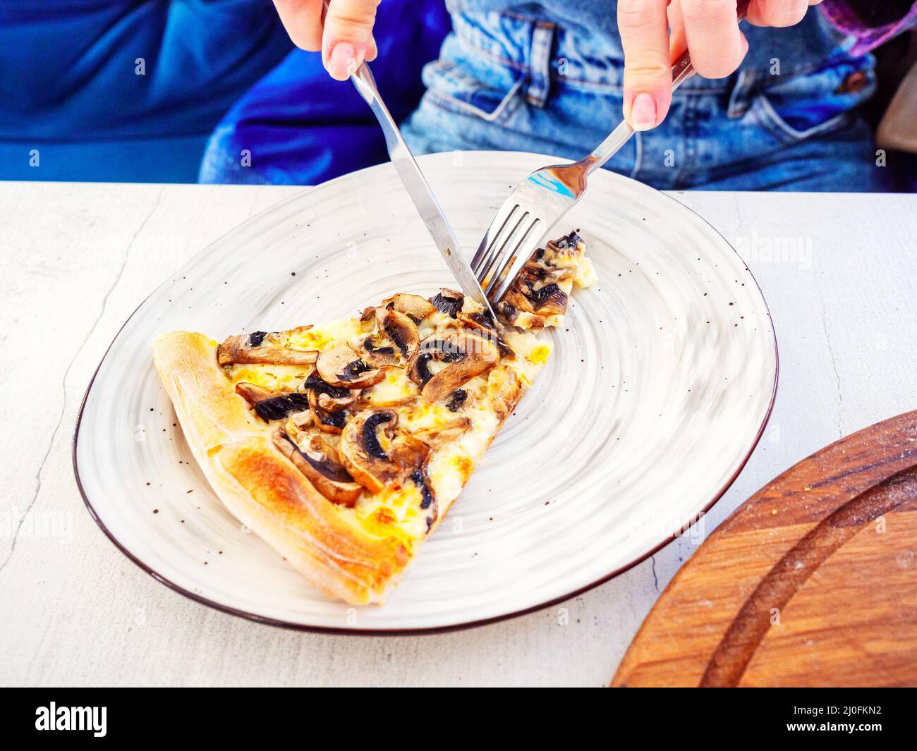 Finger halten eine Gabel und ein Messer, während sie ein schneiden Stück Pilzpizza auf einem Teller liegend Stockfoto