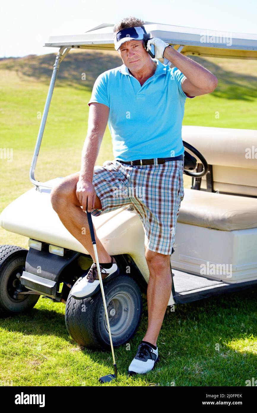 Anrufe von seinem mobilen Büro aus tätigen. Ein reifer Golfer, der neben seinem Golfwagen steht und auf seinem Handy spricht. Stockfoto