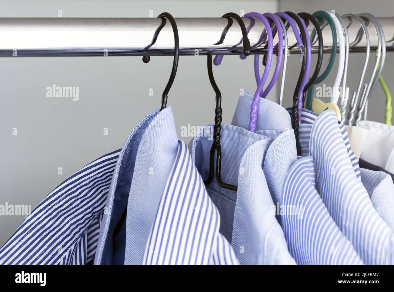 Gruppe von hellblau gestreiften Hemden, die an der Stange einer weißen Garderobe hängen. Stockfoto