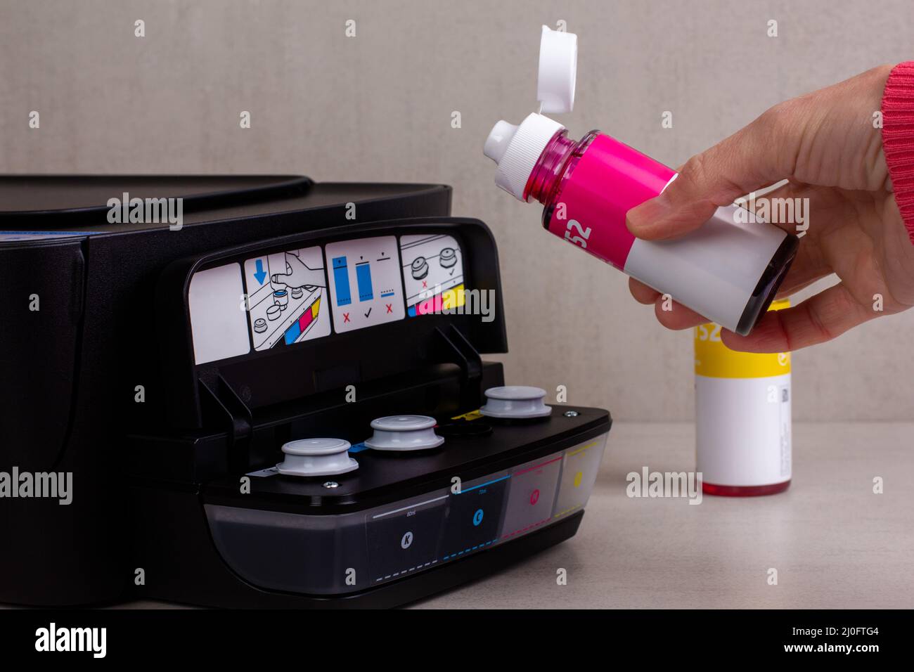 Die Hand einer Frau gießt Farbe aus einer Flasche in den Drucker Stockfoto