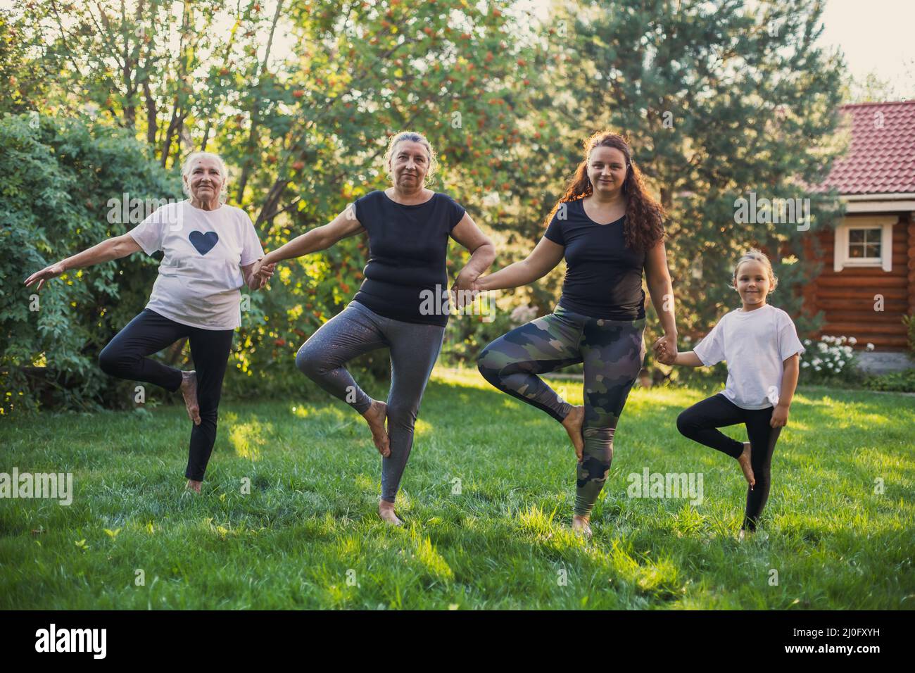 Glückselige Frauen aus vier Generationen einer Familie, die auf einem Bein stehen und sich die Hände auf einer grünen Wiese wärmen. Zeit verbringen Stockfoto