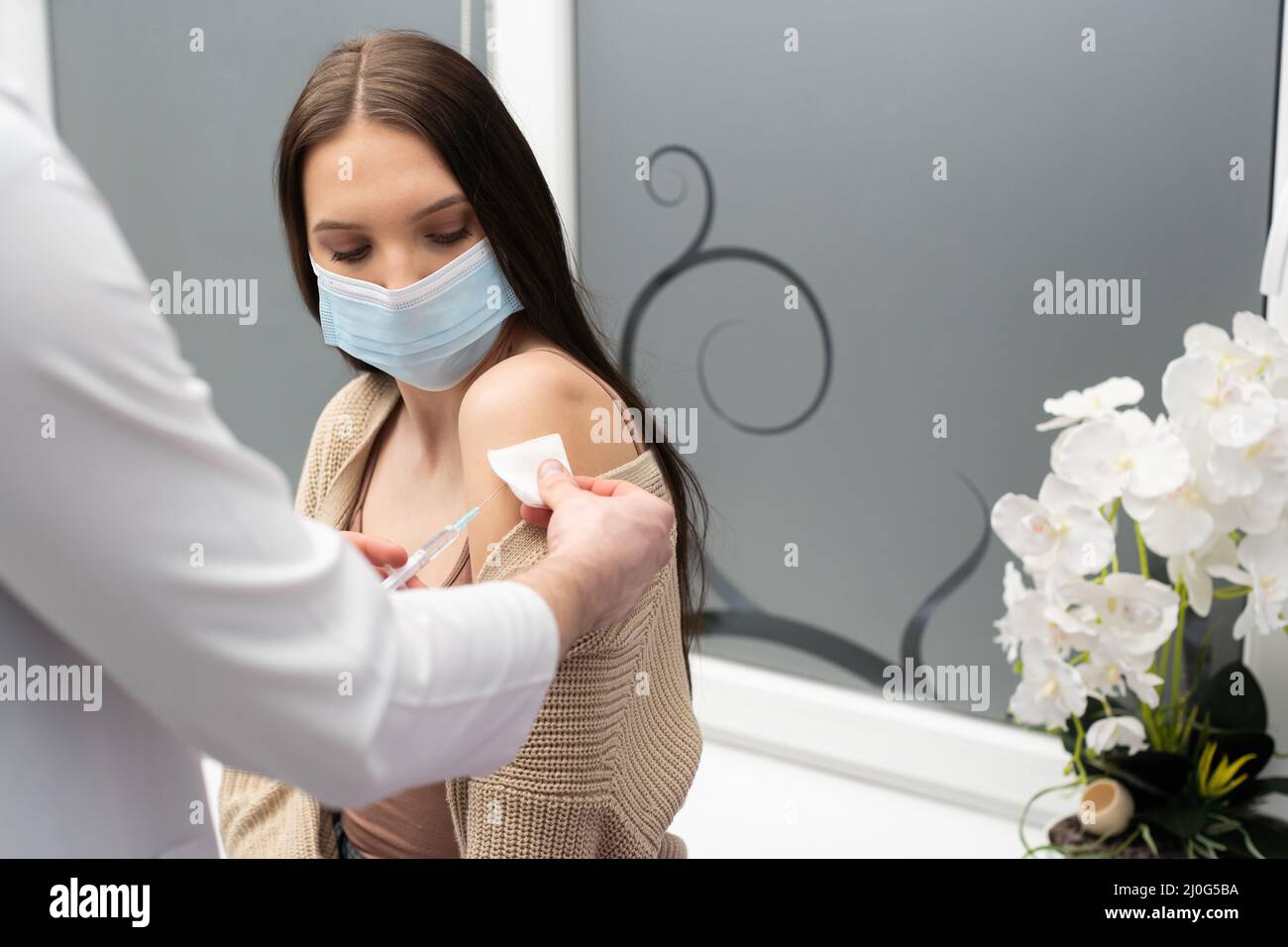 Ein Arzt von der Krankenhausabteilung steckt eine Nadel in den Arm, um einem jungen Patienten den Impfstoff COVID19 zu verabreichen. Ein steriler Arzt Stockfoto