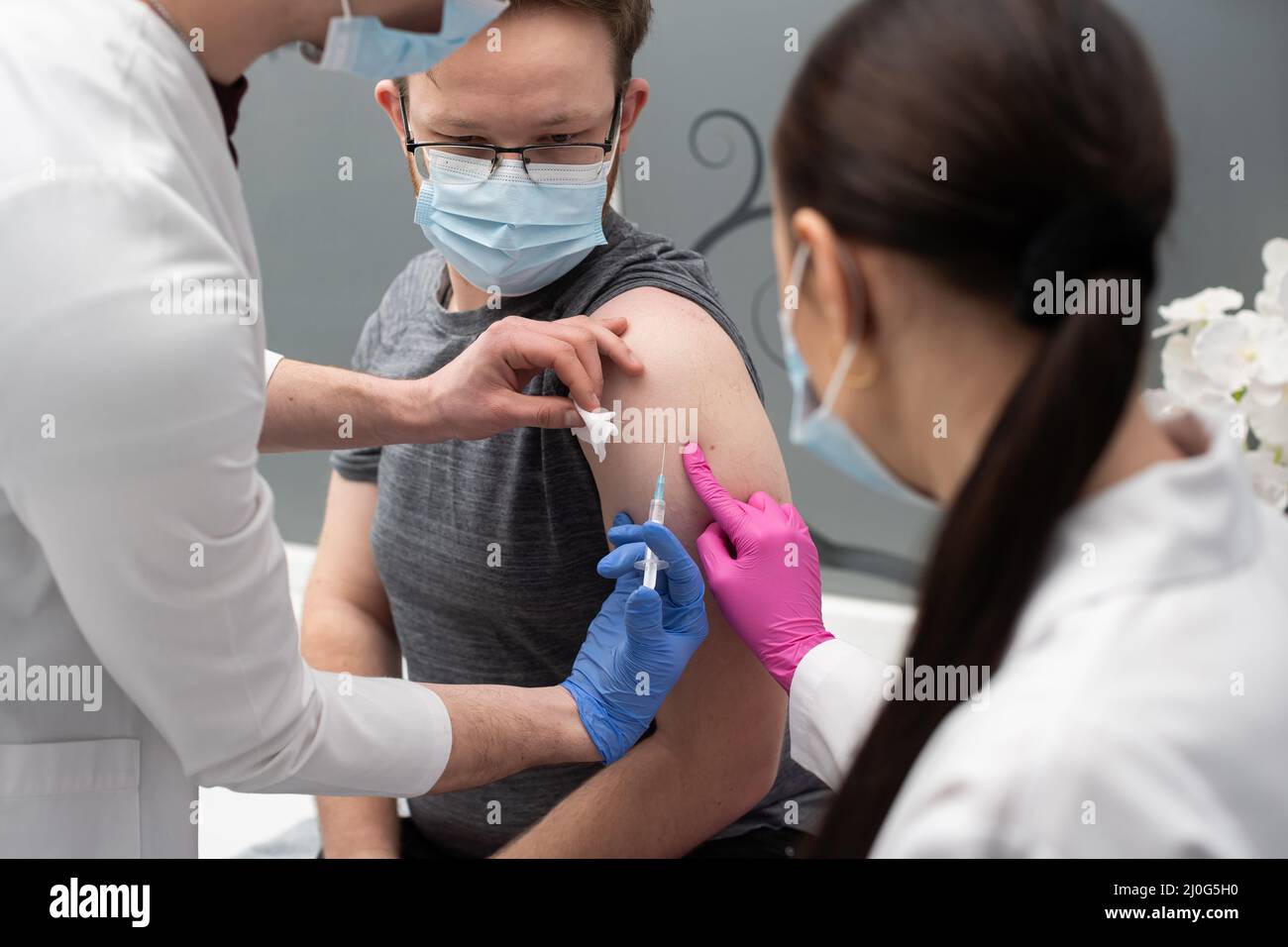 Ein junger Praktikant lernt, einem jungen erwachsenen Patienten einen COVID19-Impfstoff zu injizieren. Eine sterile Arztpraxis in einer Privatklinik. A y Stockfoto