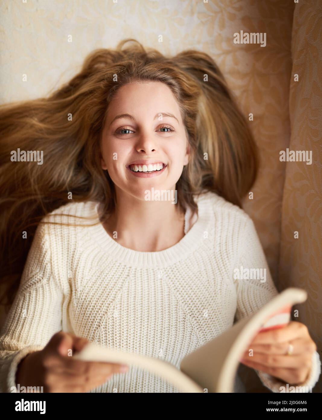 Lesen ist mein Lieblingshobby. Porträt einer attraktiven jungen Frau, die ein Buch liest, während sie zu Hause auf dem Sofa liegt. Stockfoto
