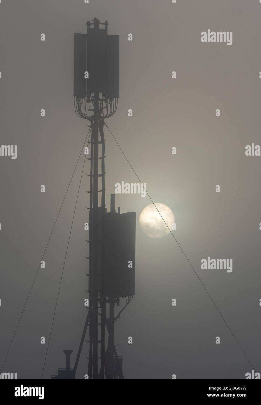 Kommunikationsturm auf einem Gebäude mit 4G 5G Antenne bei Sonnenaufgang im Nebel. Stockfoto