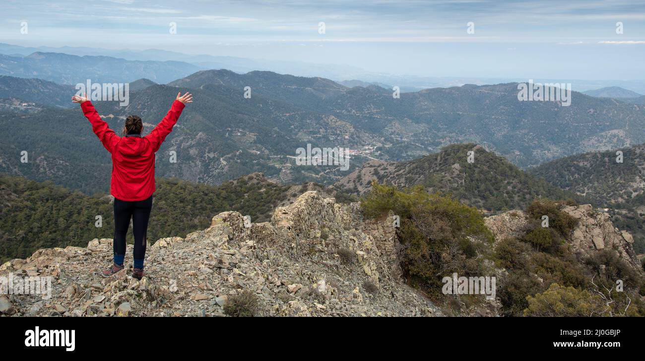 Rückansicht einer Backpacker-Frau mit erhobenen Armen auf felsigen Gipfel stehend und Bergpanorama genießen. Stockfoto