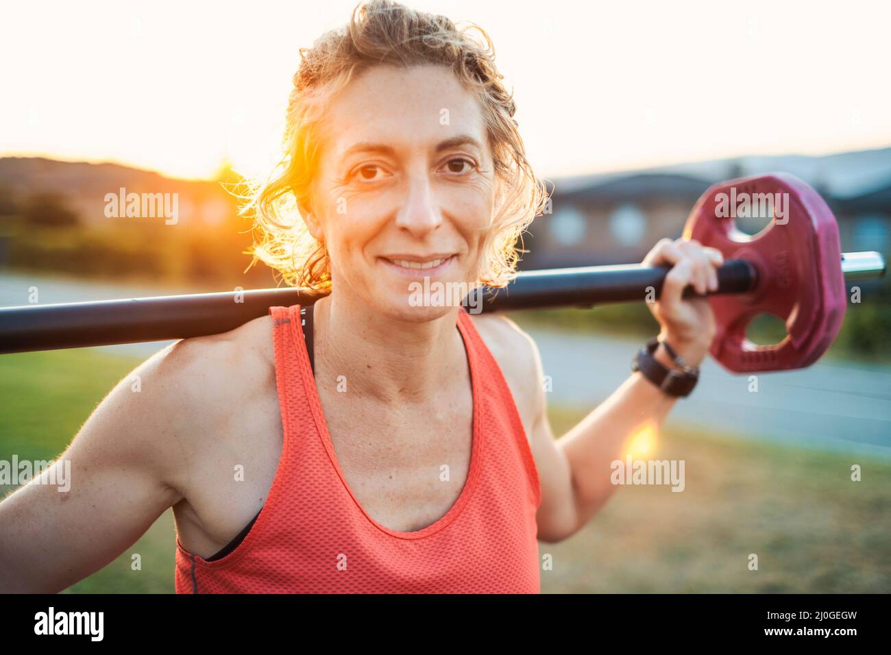 Echte junge reife kaukasische Frau in einem Sport tragen im Park mit einem Gewichtheben bar. Fitnesskonzept. Stockfoto