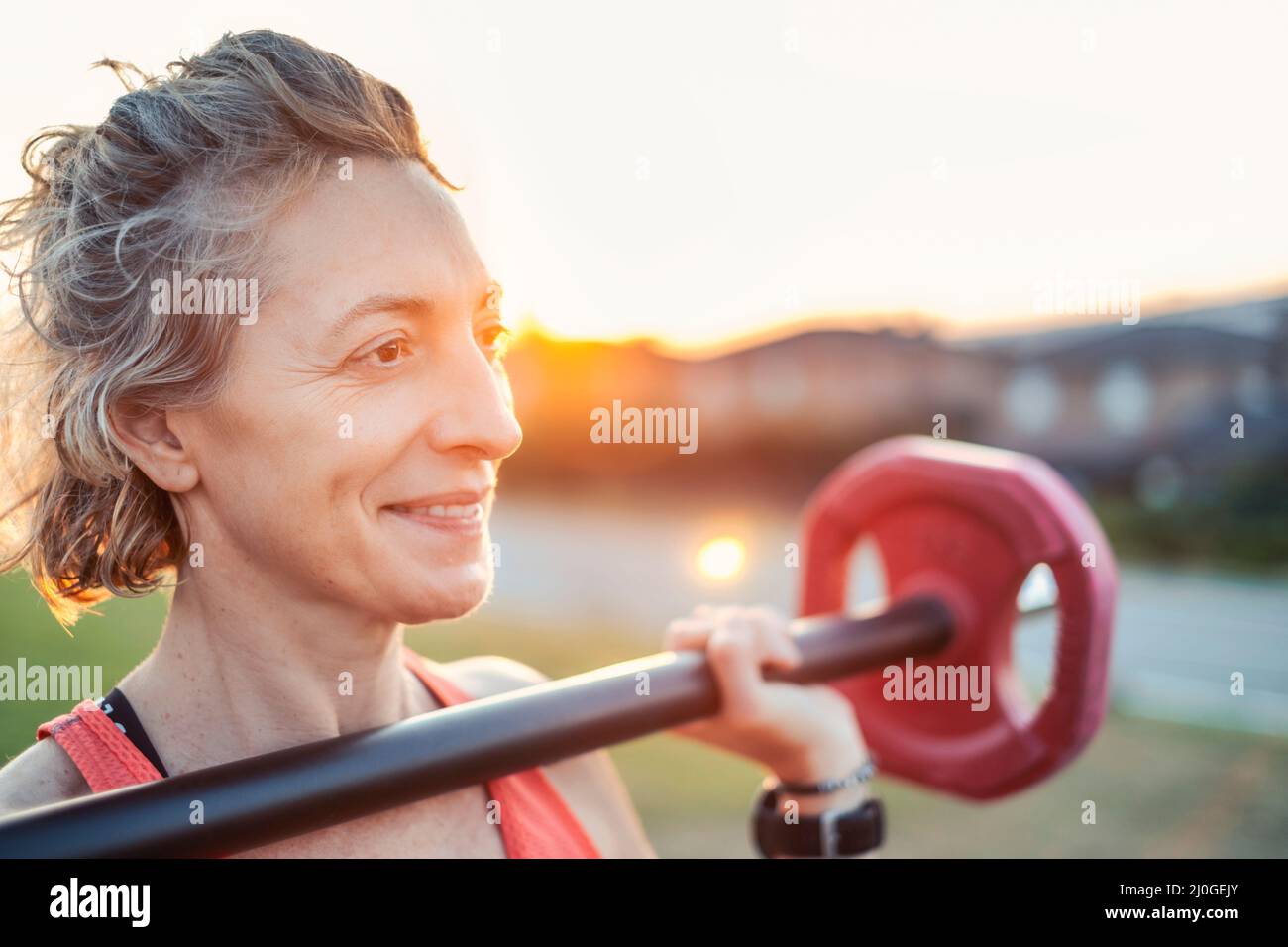 Echte junge reife kaukasische Frau in einem Sport tragen im Park mit einem Gewichtheben bar. Fitnesskonzept. Stockfoto