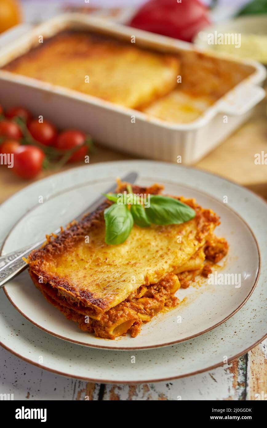 Hausgemachte leckere Fleischlasagne mit frischem Basilikum und Parmesankäse In einem Teller auf Holzgrund Stockfoto