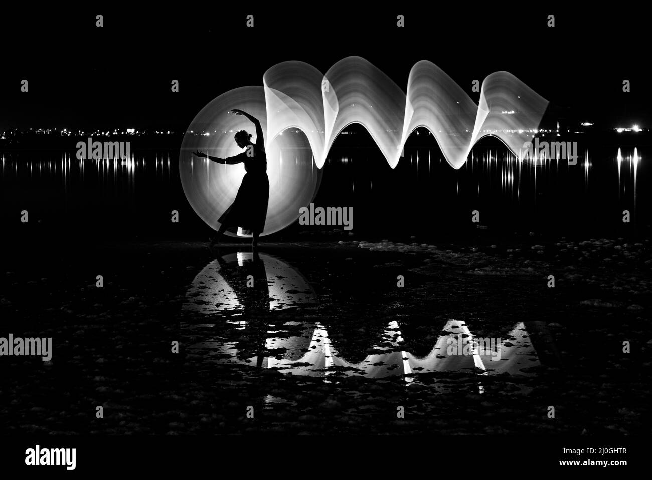 Silhouette einer Frau, die draußen an einem See tanzt, mit malendem Licht und Reflexionen auf dem Wasser. Stockfoto