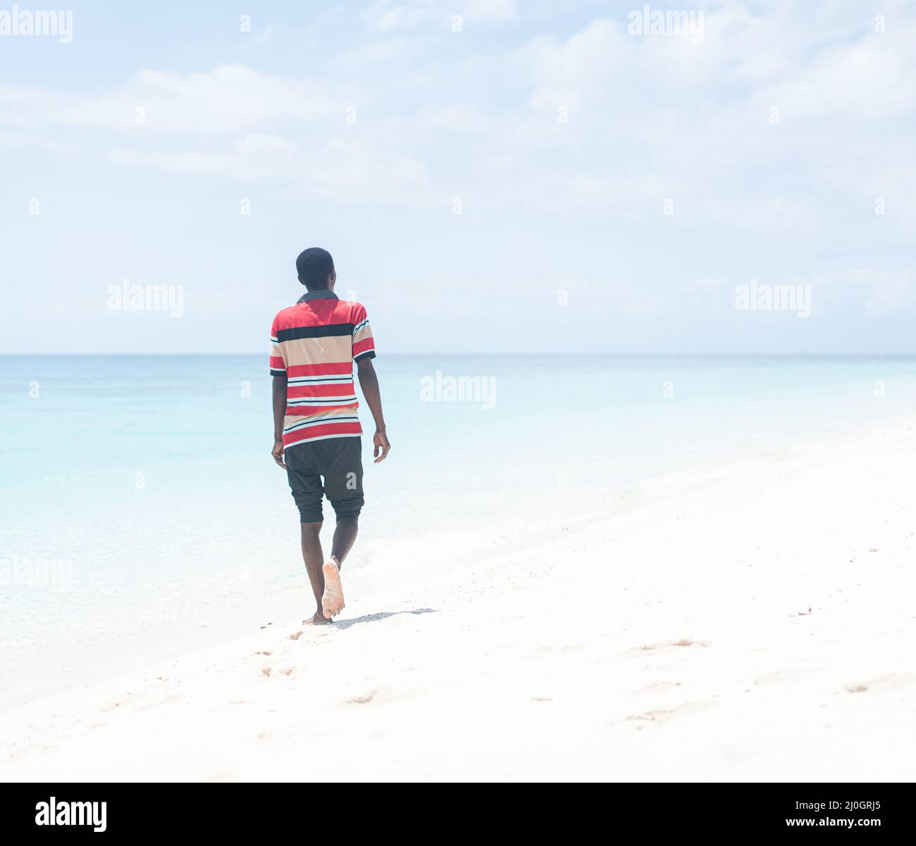 Schwarzer afrikanischer junger Mann, der am tropischen Strand spazierengeht Stockfoto