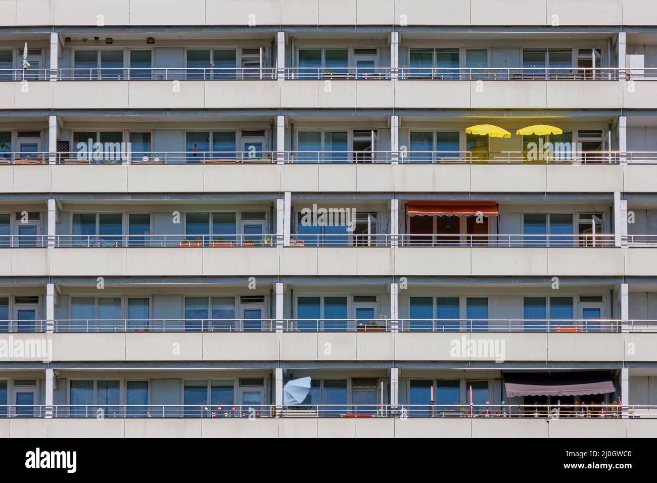 Fassade eines großen Mehrfamilienhauses mit gelben Sonnenschirmen auf einem der Balkone Stockfoto