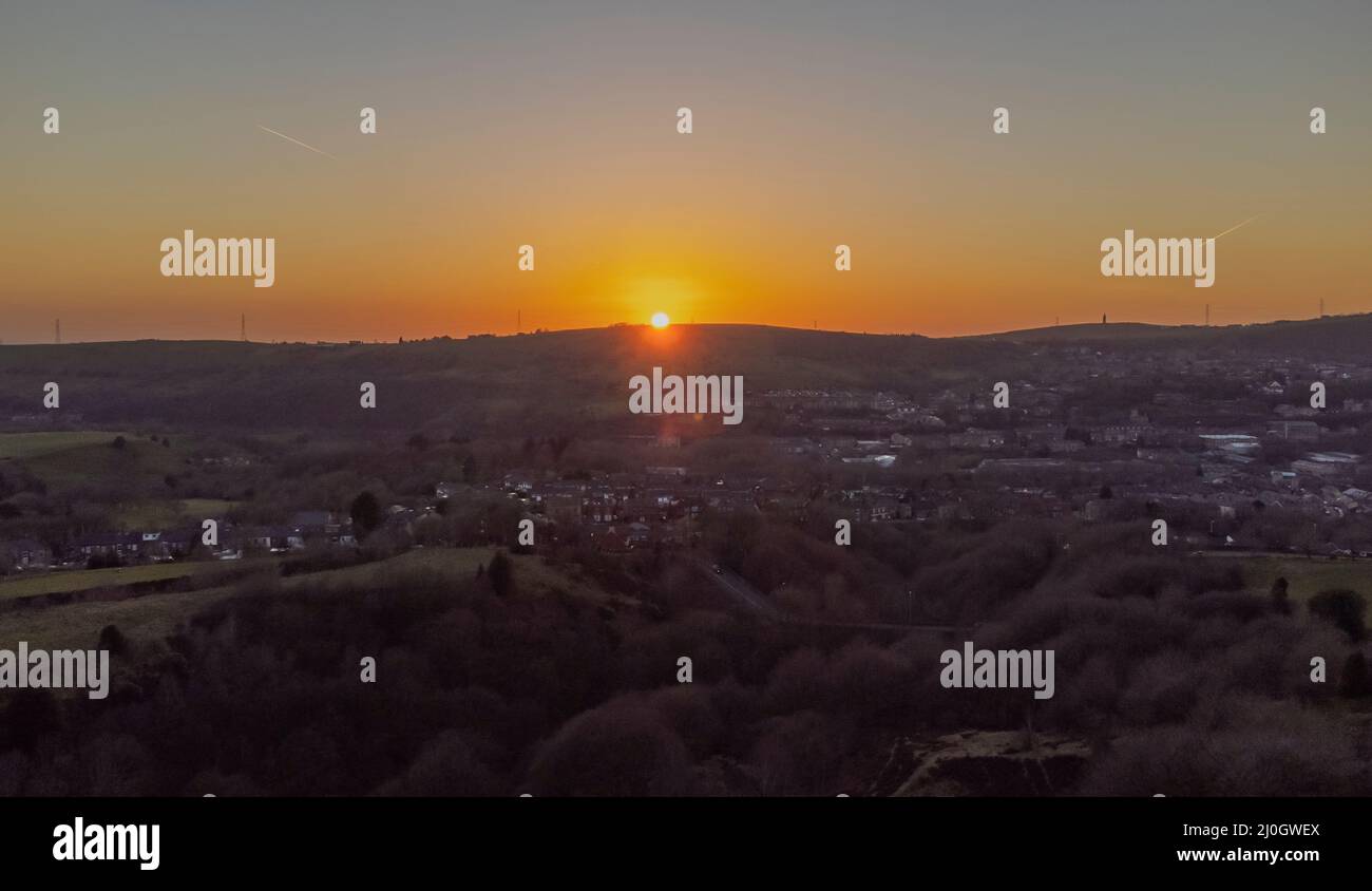 Luftaufnahme zeigt Hartshead Pike, wie die Sonne hinter einem Hügel über dem Dorf Mossley im Großraum Manchester untergeht Stockfoto