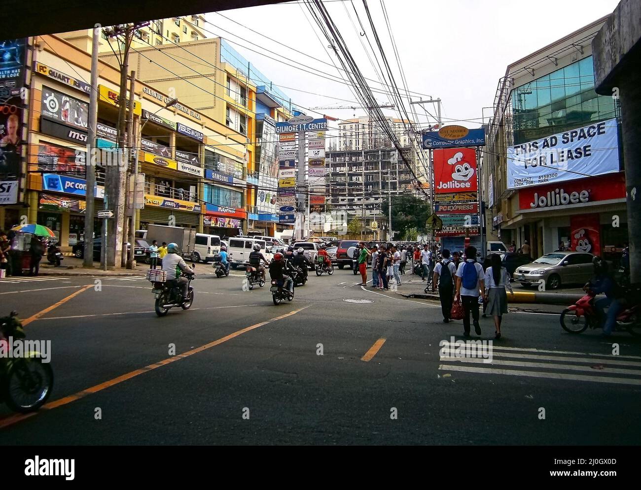 Eine belebte Straße mit Motorradverkehr und Leuten, die durch die Geschäfte in Quezon City laufen Stockfoto