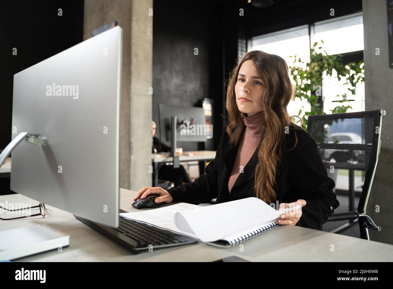 Design- und Architekturthema. Eine junge Architektin arbeitet in einem modernen Büro an einem Projekt mit Bauplänen am Computer Stockfoto