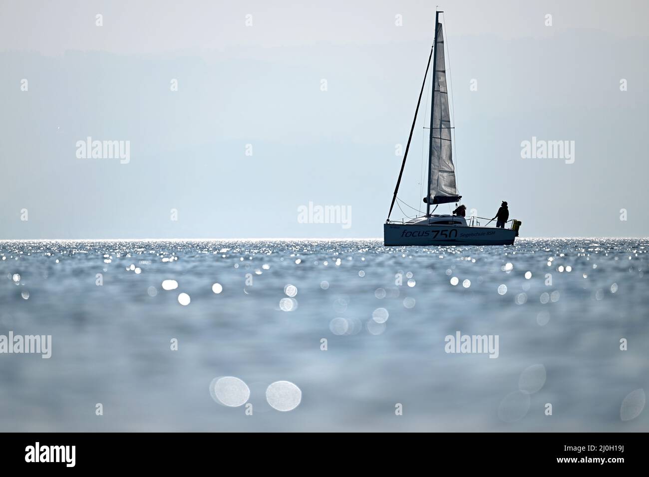 Langenargen, Deutschland. 19. März 2022. Vor Langenargen segelt ein Boot auf dem Bodensee, während im Vordergrund die Sonne im Wasser glitzert. Quelle: Felix Kästle/dpa/Alamy Live News Stockfoto