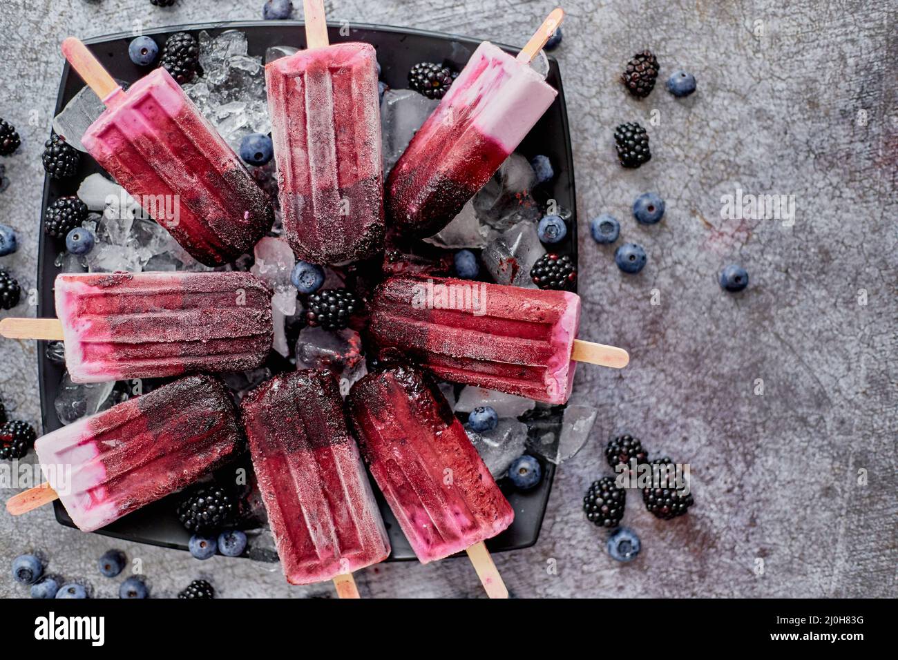 Hausgemachte frische gefrorene Heidelbeere und Brombeerpopsicles auf schwarzem Teller mit Eis auf Stein sitzen Stockfoto