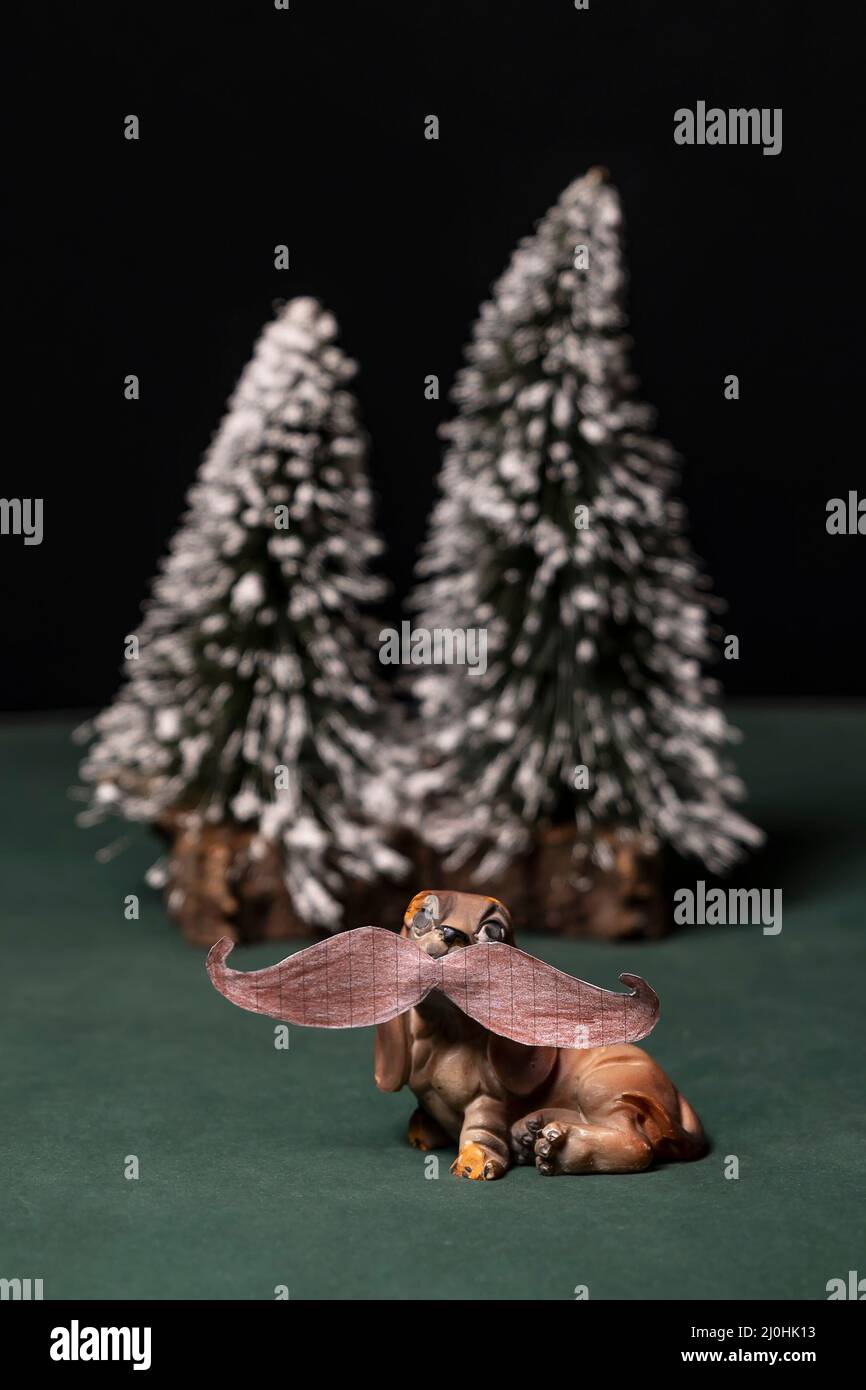 Ein Spielzeug-Hund mit einem menschlichen Schnurrbart auf Papier gezeichnet, mit verschneiten Bäumen im Hintergrund Stockfoto