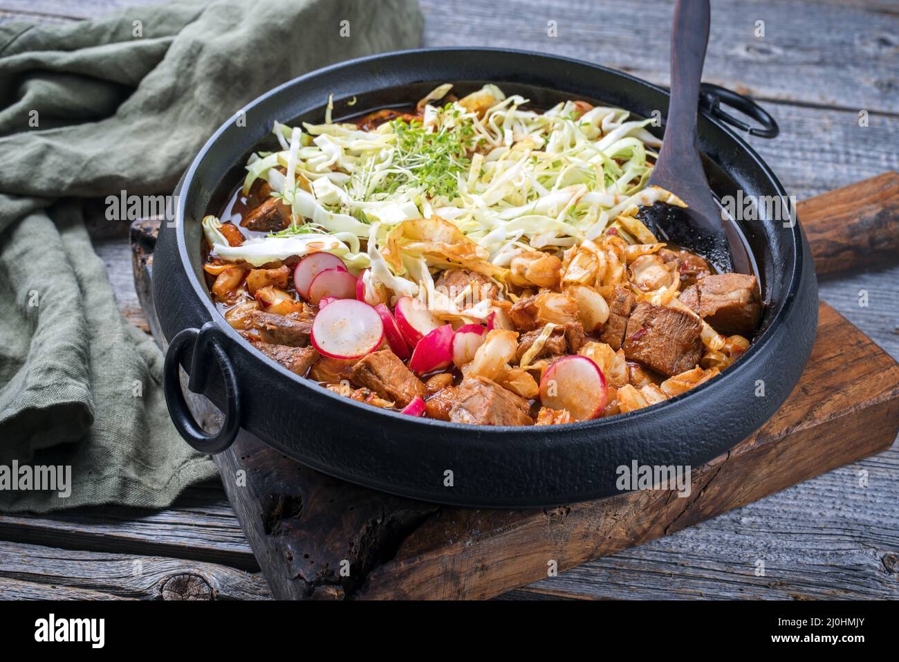 Traditionelle, langsam gekochte mexikanische Pozole rojo-Suppe mit Schweinefleisch und heimeliger Maiz, die als Nahaufnahme in einem modernen Design aus Gusseisen serviert wird Stockfoto