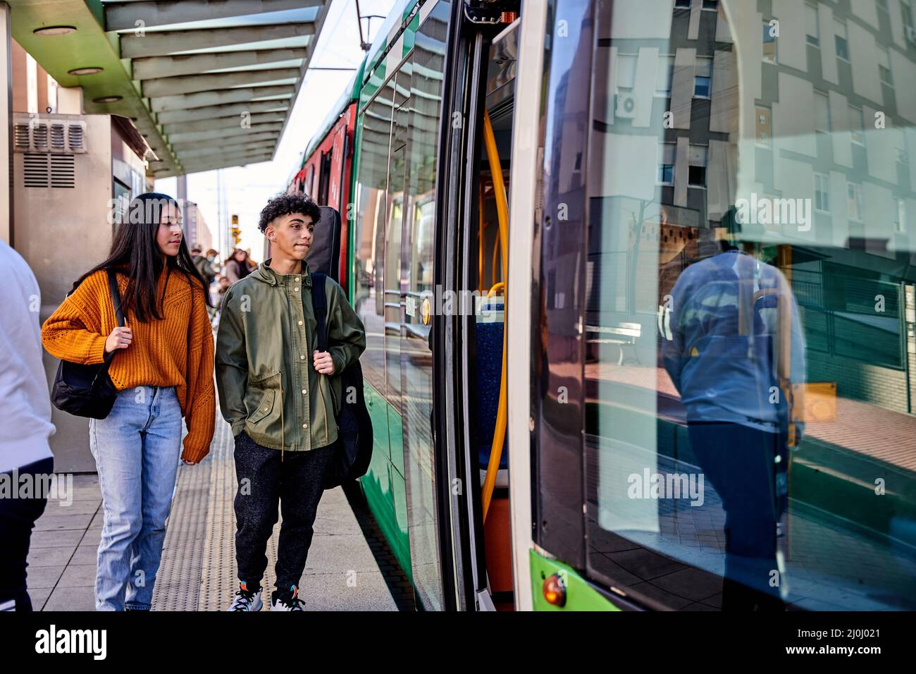 Seitenansicht von jungen lateinamerikanern, die in eine Straßenbahn einsteigen. Paar Musiker mit Instrumenten auf dem Rücken. Gitarre und Ukulele. Transportkonzept. Stockfoto