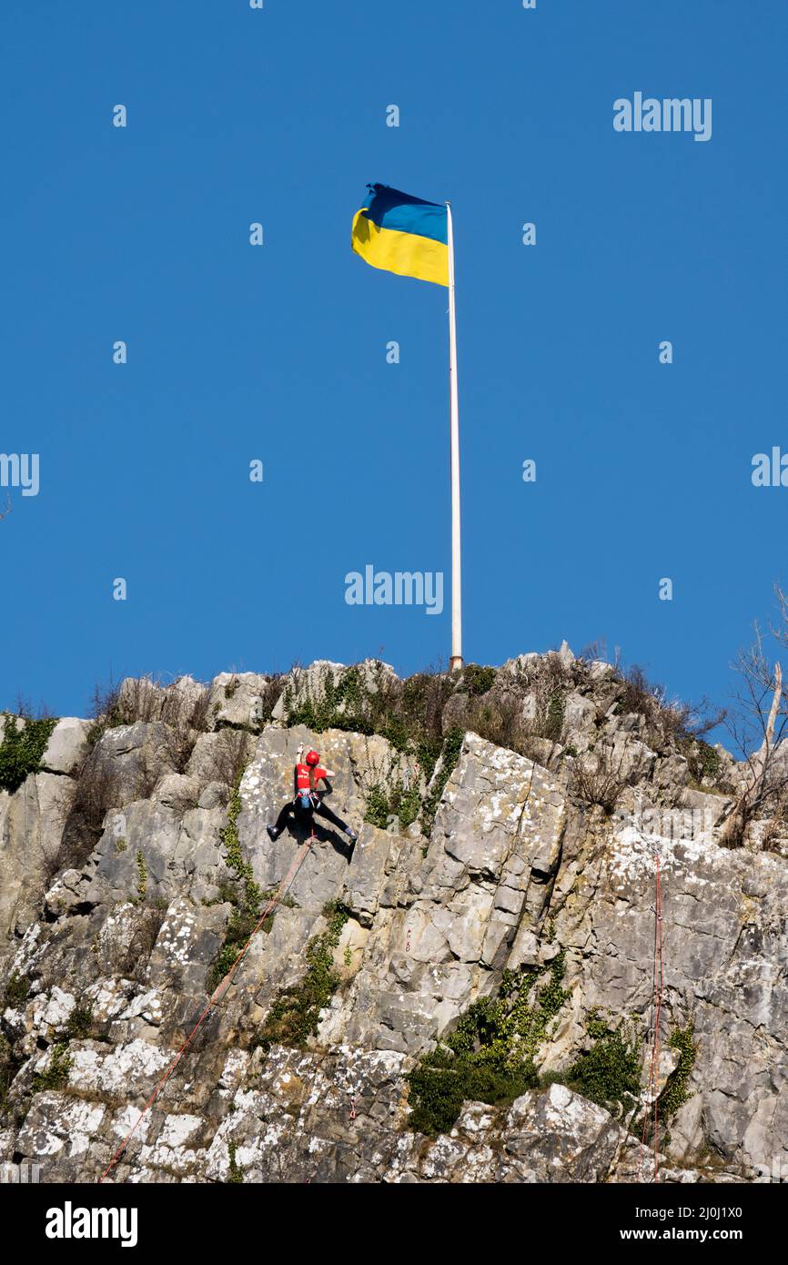 Während ein Bergsteiger aufsteigt, fliegt die Ukraine-Flagge auf Castleberg Crag über der kleinen Stadt Settle in Yorkshire Dales. Quelle: John Bentley/Alamy Live News Stockfoto
