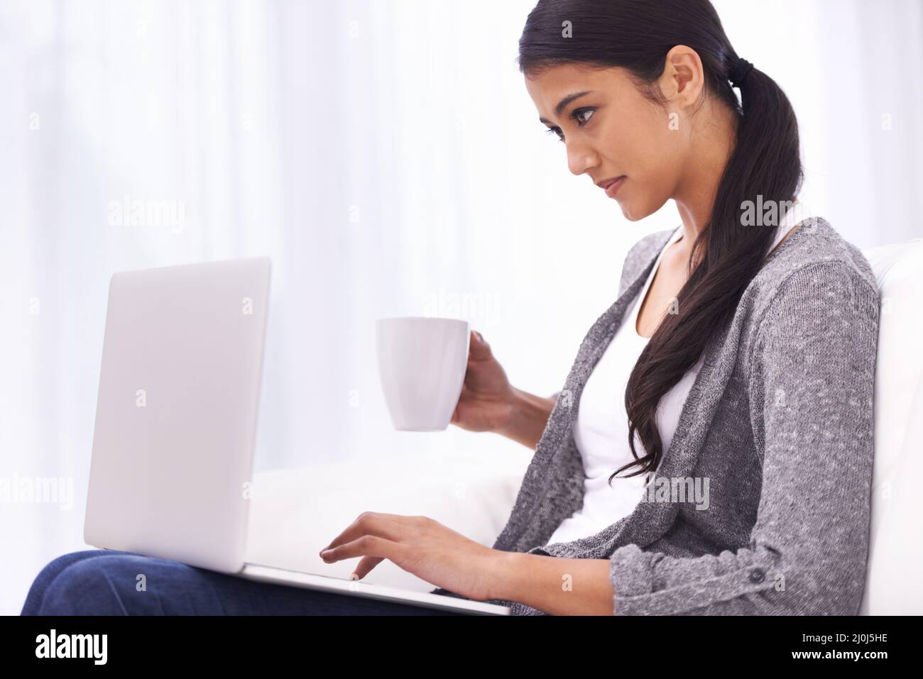 Ich hole ihre E-Mails ein. Eine wunderschöne junge Frau, die im Internet surft und dabei eine Tasse Kaffee genießt. Stockfoto
