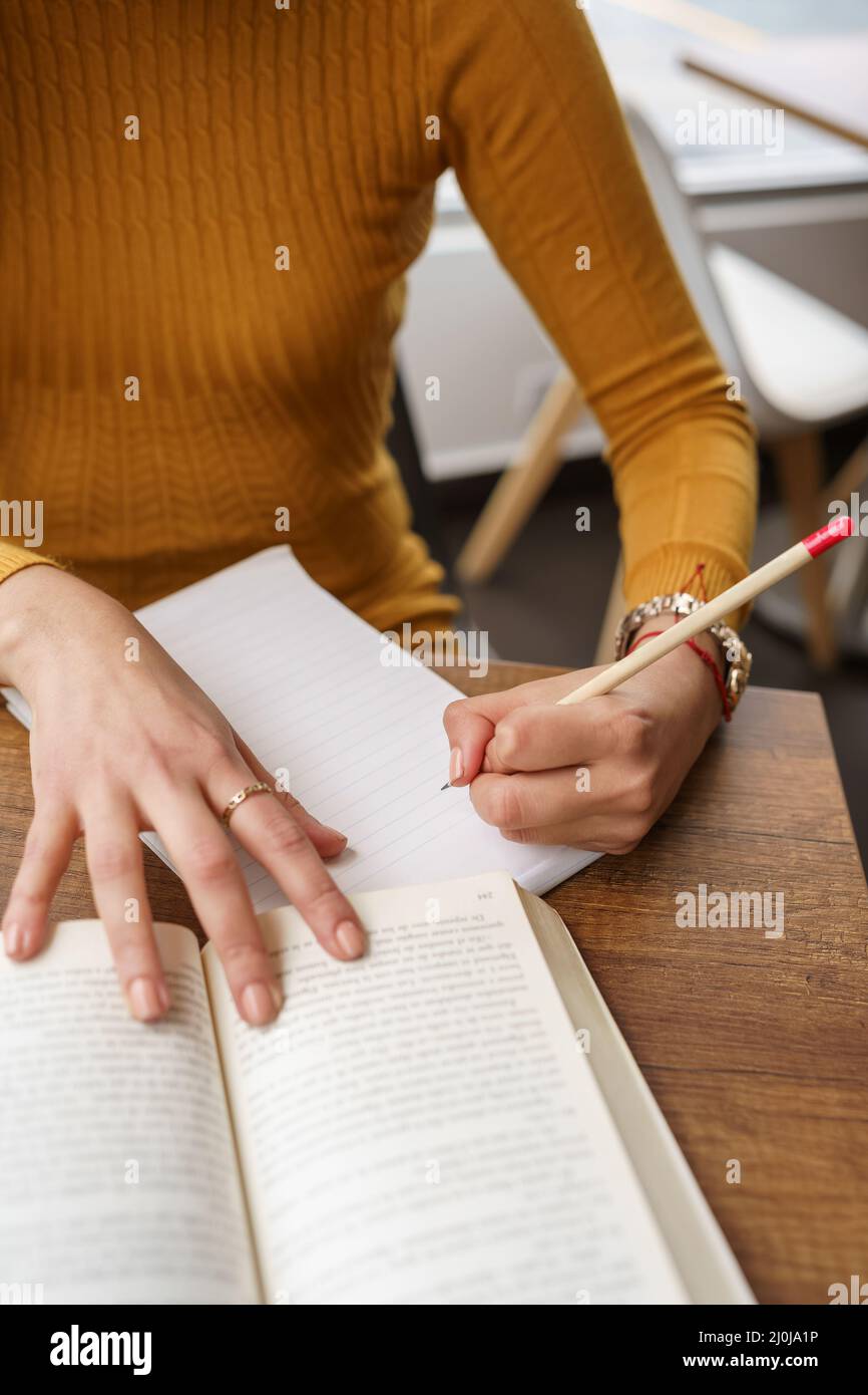Details über die Hand einer Person, die einen Bleistift hält, um Notizen auf einem Blatt eines Buches zu machen, intellektuelle Arbeit und Mühe, Hausaufgaben zu erfüllen Stockfoto