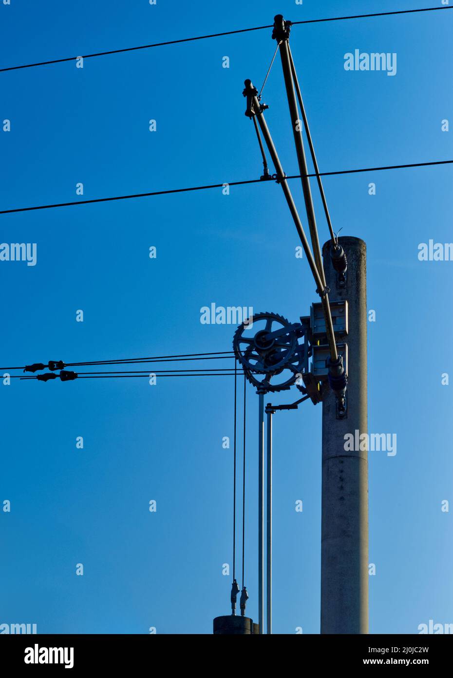 Zahnräder eines elektrischen Schaltgetriebes auf einem Eisenbahnmast in klarem blauen Himmel Stockfoto