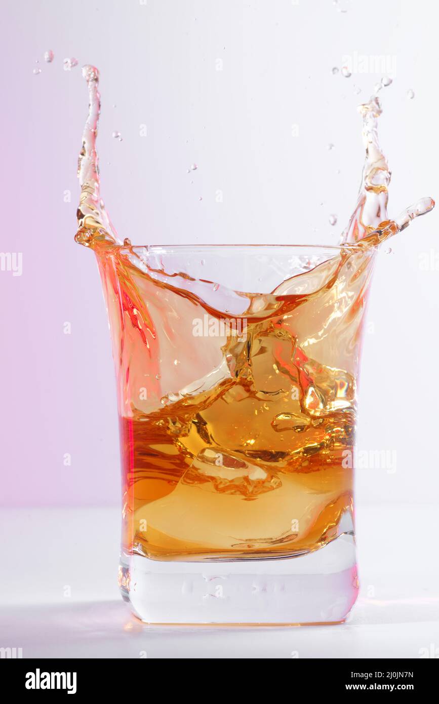 Glas alten Whiskys mit Eis. Ein spritzendes Glas Whiskey mit Eis auf einem hellen Hintergrund isoliert Stockfoto