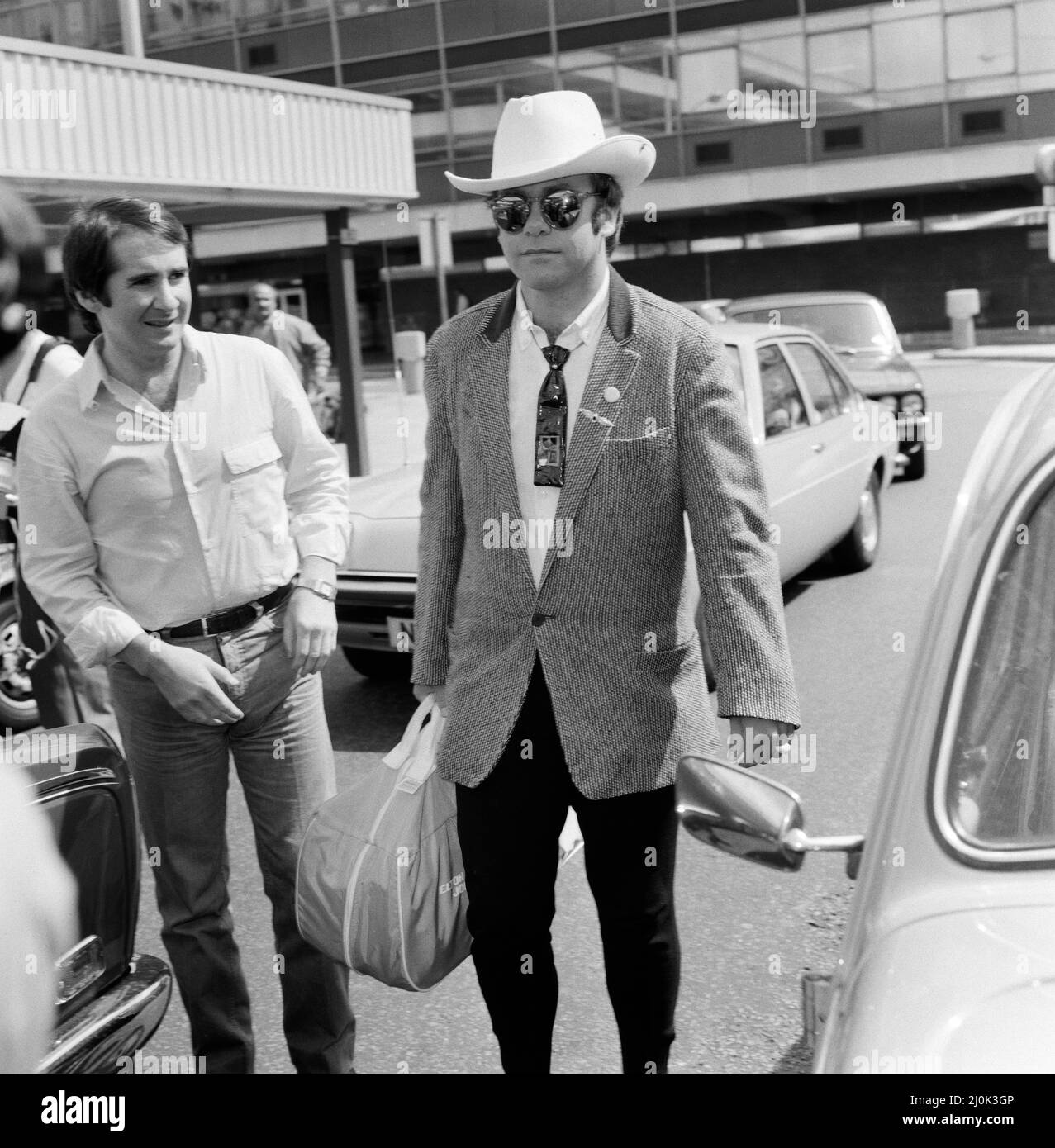 Mit einem stetson-Hut bekleidet verlässt Elton John den Flughafen Heathrow nach Amerika. Auf der linken Seite ist John Reid, der Manager von Elton. 10.. August 1980. Stockfoto