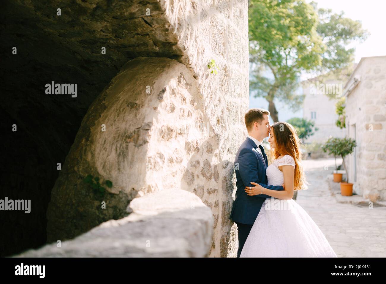 Die Braut und der Bräutigam umarmen sich in einer schönen alten Straße von Perast, der Bräutigam küsst die Braut auf die Stirn Stockfoto