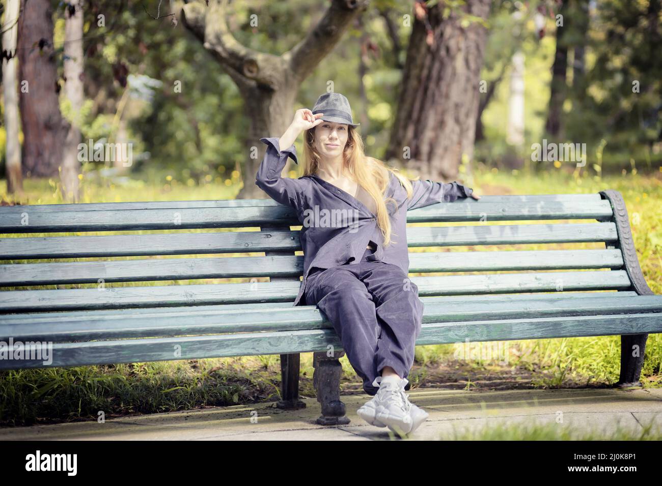 Eine Frau in Fliederkleidung und einem Hut sitzt an einem sonnigen Tag auf einer Parkbank Stockfoto