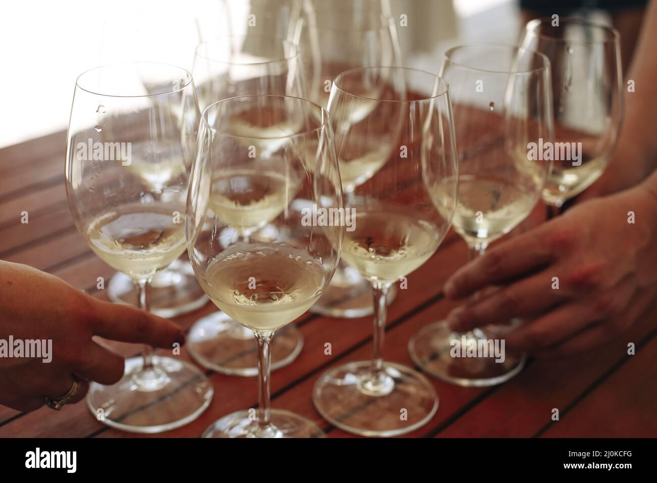 Gläser mit verschiedenen Weinsorten und menschlichen Händen, die Weingläser im Hintergrund halten Stockfoto
