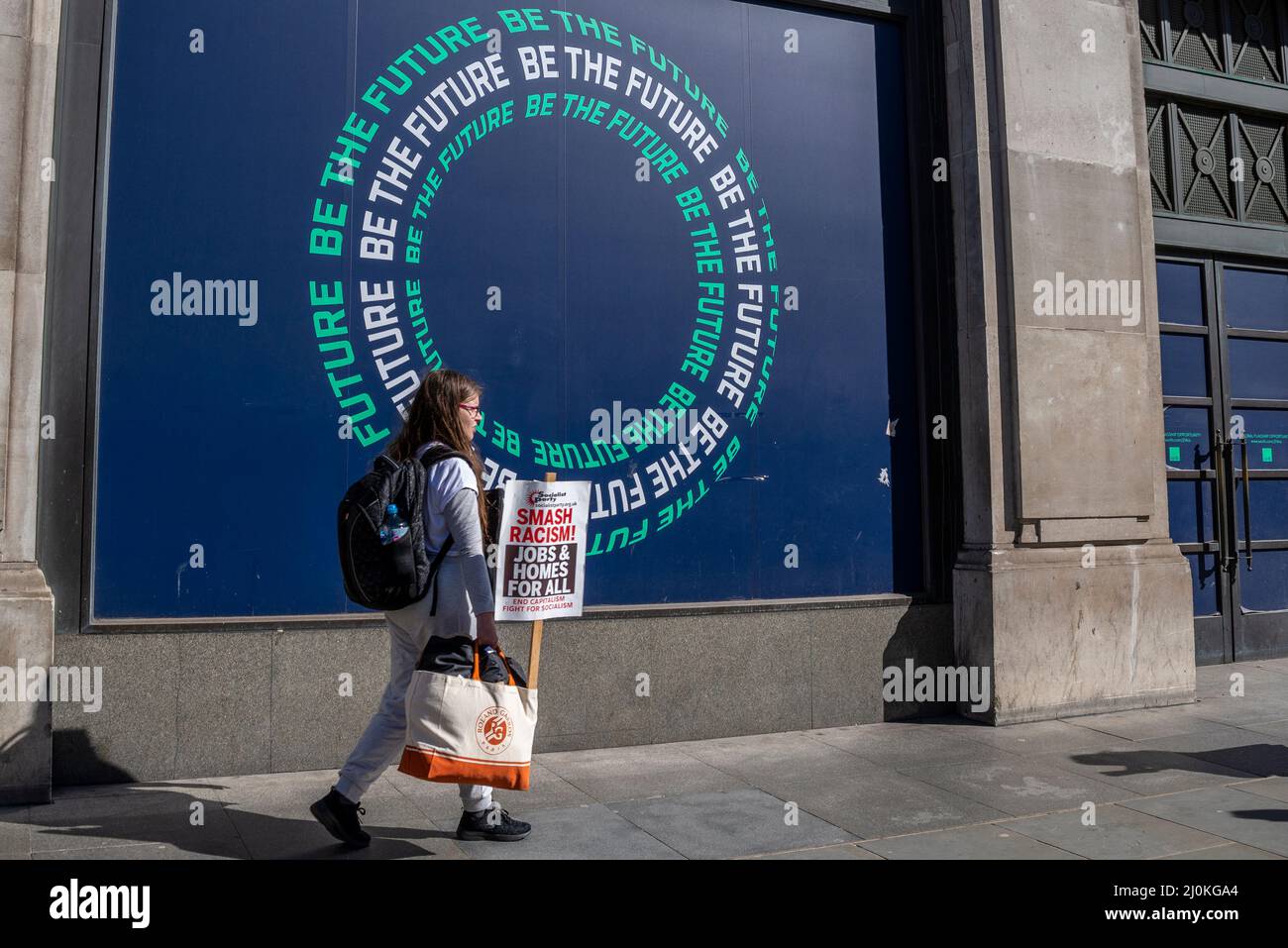 Protest am UN-Tag gegen Rassismus in London. Die junge Protesterin geht zum marsch, vorbei an einem Schaufenster, das sagt, sei die Zukunft Stockfoto