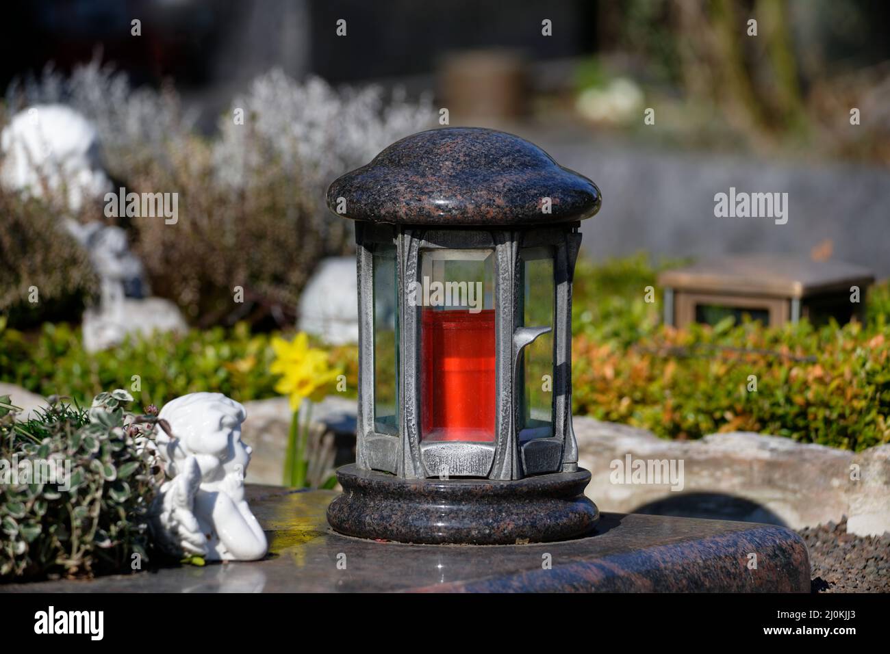 Grablaterne mit roter Kerze auf einem Grab im Sonnenschein Stockfoto