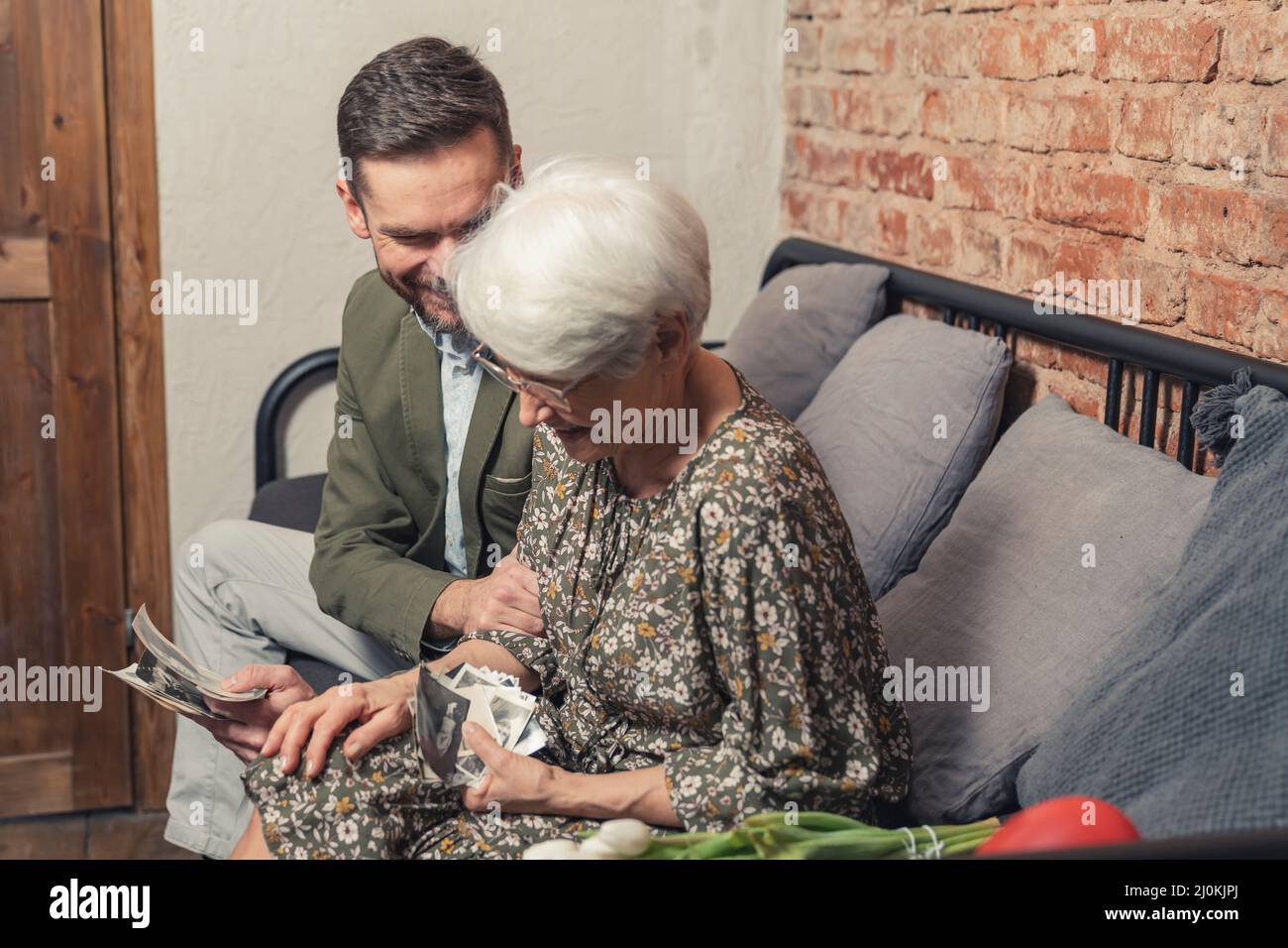 Die Mutter der europäischen Rentnerin lacht laut, während sie alte Fotos ansieht und mit ihrem Sohn mittleren Alters den Muttertag feiert. Hochwertige Fotos Stockfoto