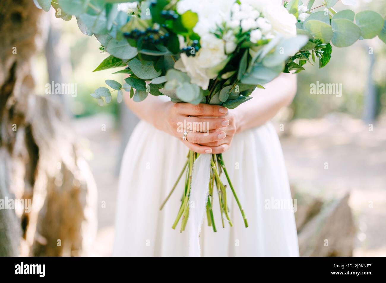 Die Braut hält einen Brautstrauß aus Rosen, Eukalyptuszweigen, zarten weißen Blumen und dunklen Beeren in ihren Händen, clos Stockfoto