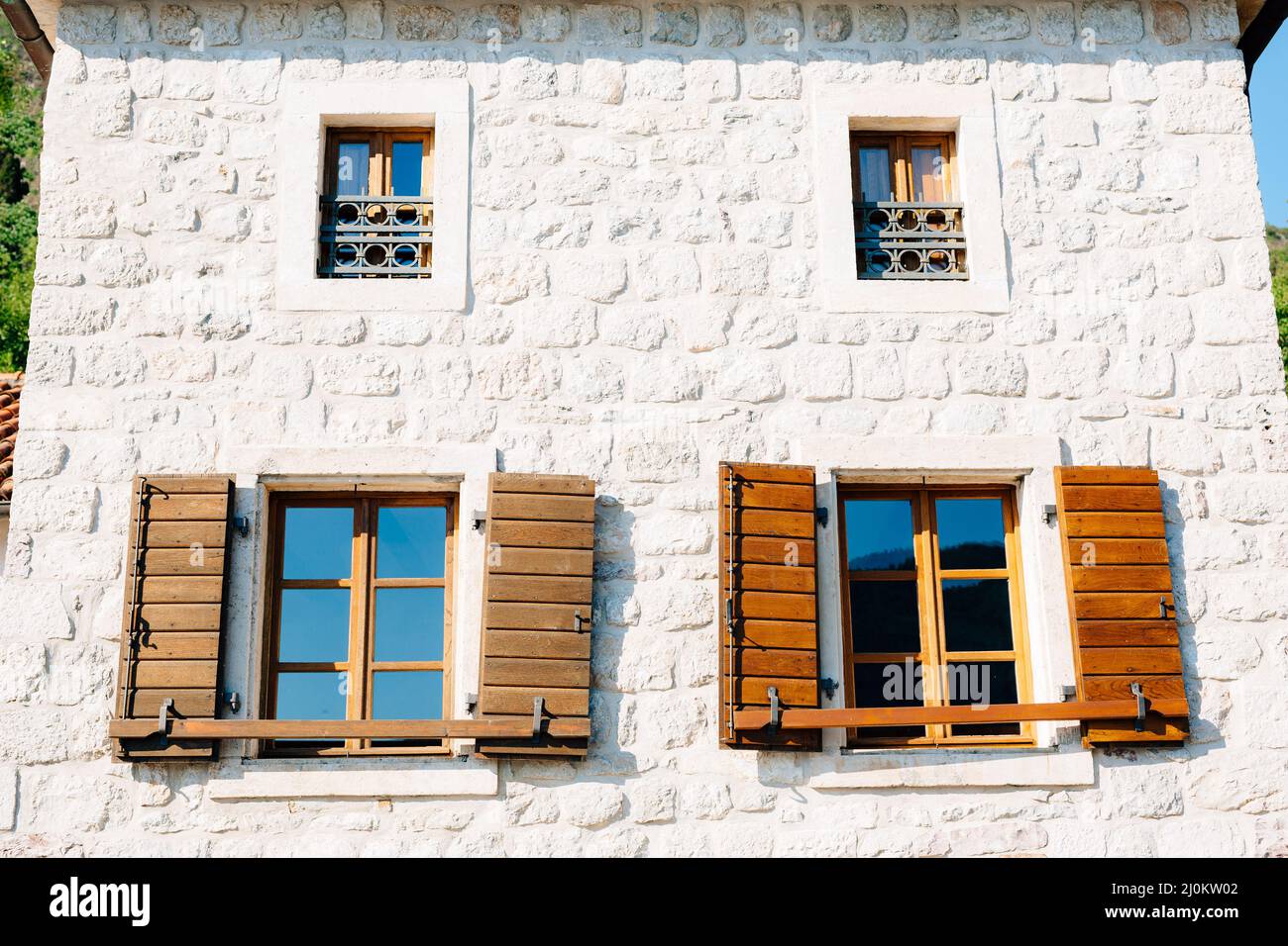 Das Haus ist aus weißem Ziegelstein mit großen Fenstern und hölzernen Fensterläden unten und kleinen Fenstern mit Metallstangen darüber. Stockfoto