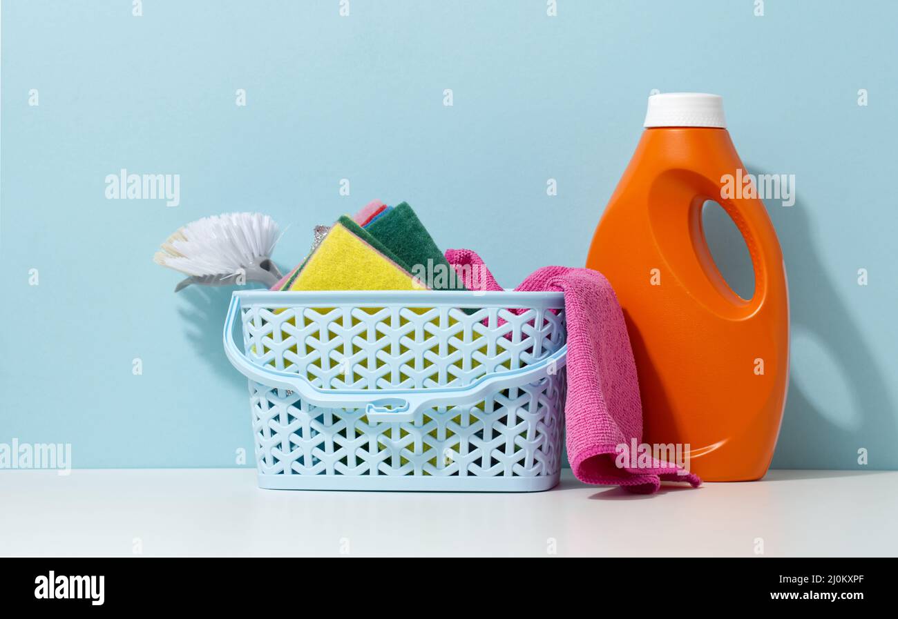 Korb mit Spucken und einer Bürste, neben einer orangen Plastikflasche mit flüssigem Reinigungsmittel auf einem weißen Tisch Stockfoto