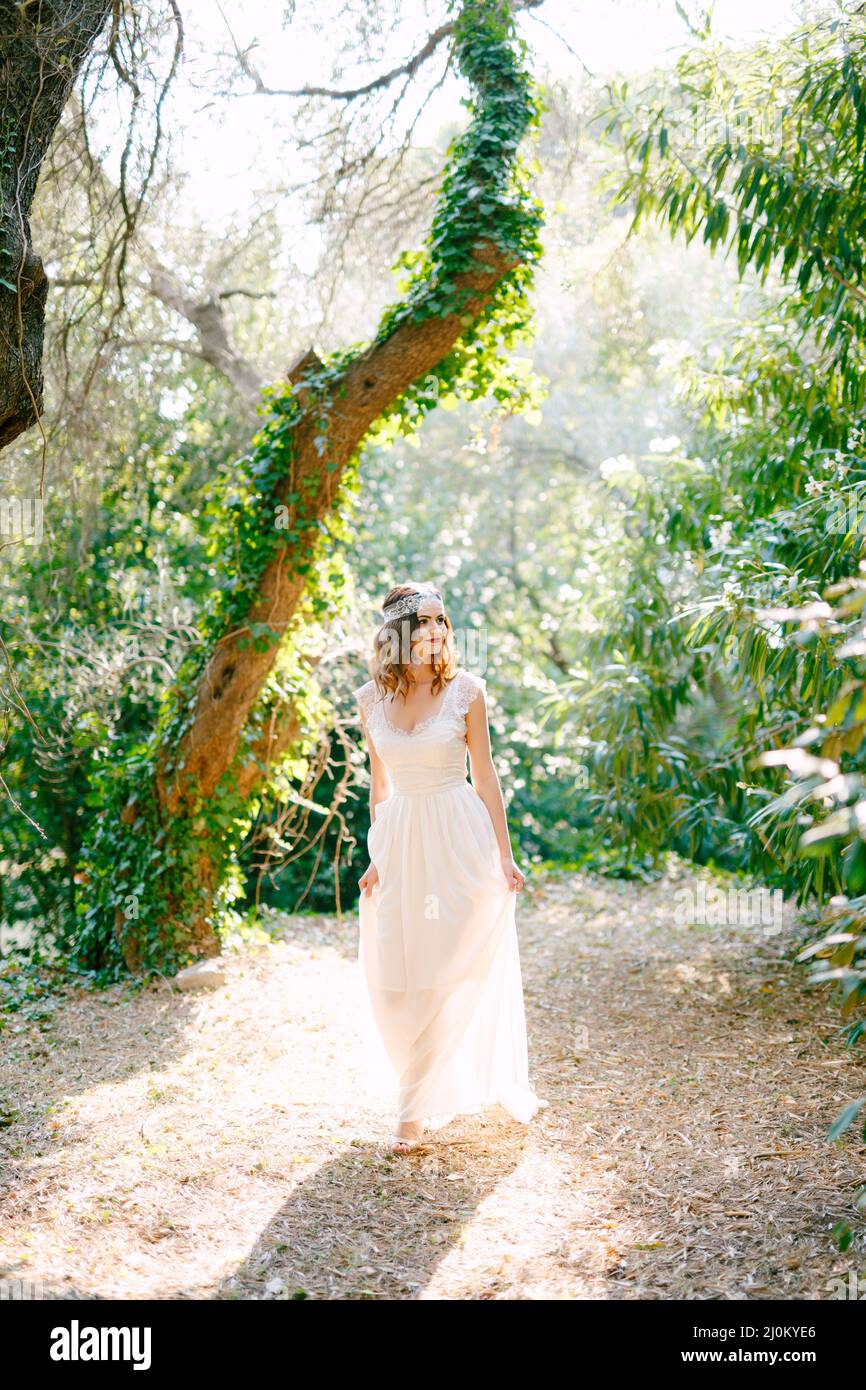 Die Braut steht in der Nähe des schönen, mit Efeu bedeckten Baumes In einem malerischen Park Stockfoto