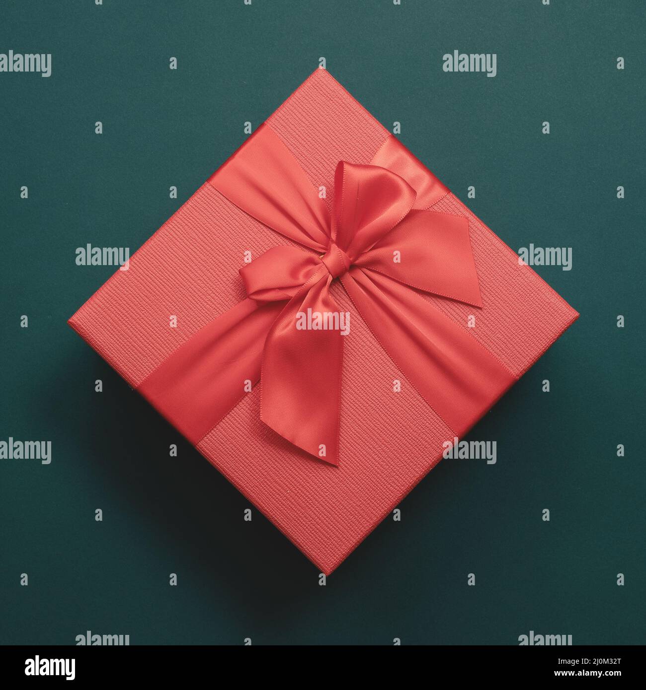 Rote Box mit Schleife auf smaragdfarbenem Hintergrund. Draufsicht. Anwesend Stockfoto