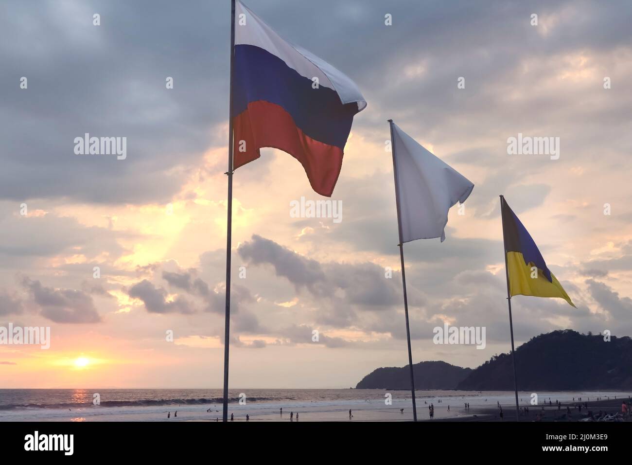 Ukrainische und russische Flaggen am Himmel bei Sonnenuntergang am Strand. Stockfoto