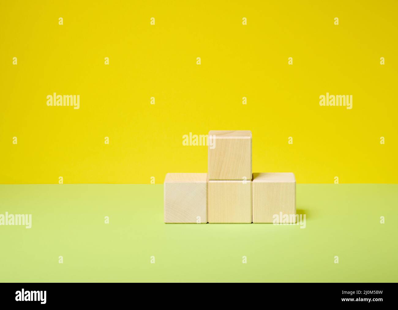 Holzwürfel auf einem Sockel auf einem gelb-grünen Hintergrund gestapelt, ein Ort, um alle Produkte Kosmetik, Lebensmittel, Getränke zu zeigen Stockfoto