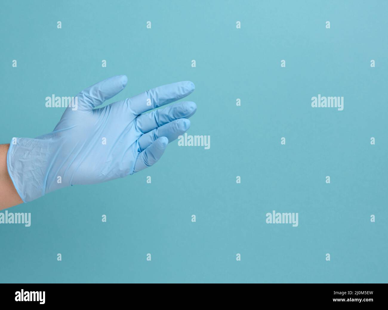 Die Hand des Arztes in einem blauen medizinischen Handschuh hält ein Objekt auf einem blauen Hintergrund Stockfoto