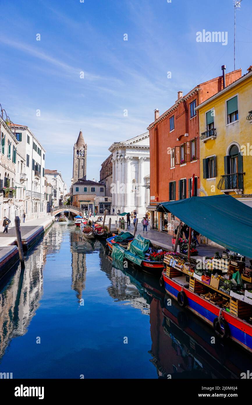 Blick auf die Kanäle von Venedig mit Kirche und einem Lebensmittelgeschäft auf einem Boot im Vordergrund Stockfoto