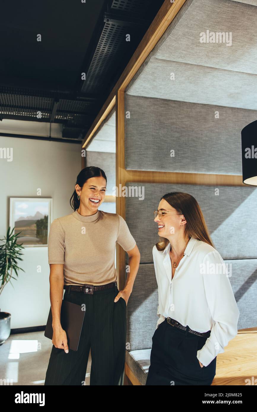 Erfolgreiche Geschäftsfrauen lachen im Büro. Zwei junge Unternehmerinnen lachen fröhlich, während sie in einem modernen Workspa zusammenstehen Stockfoto